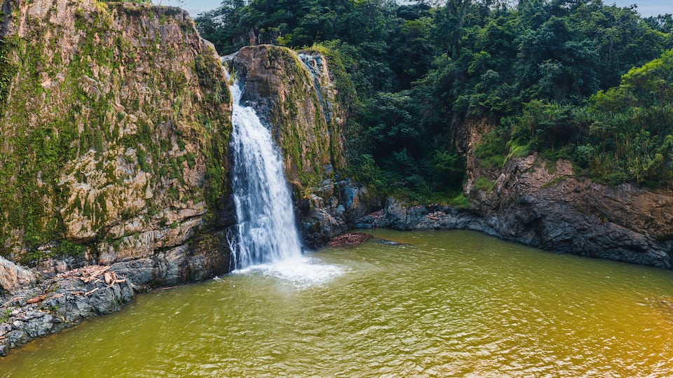 A waterfall cascading into a river surrounded by lush greenery and rocky cliffs.