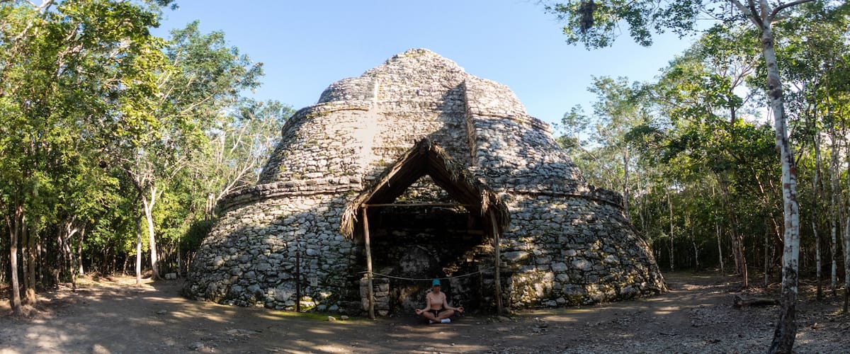 A stone structure with a thatched roof surrounded by trees.