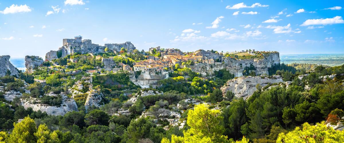 A historic town perched on a rocky cliff with lush greenery, overlooking a vast sea.