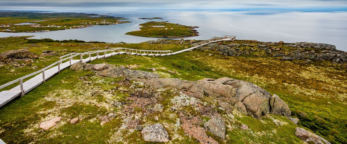 A coastal landscape with a wooden walkway, rocky terrain, and a body of water.