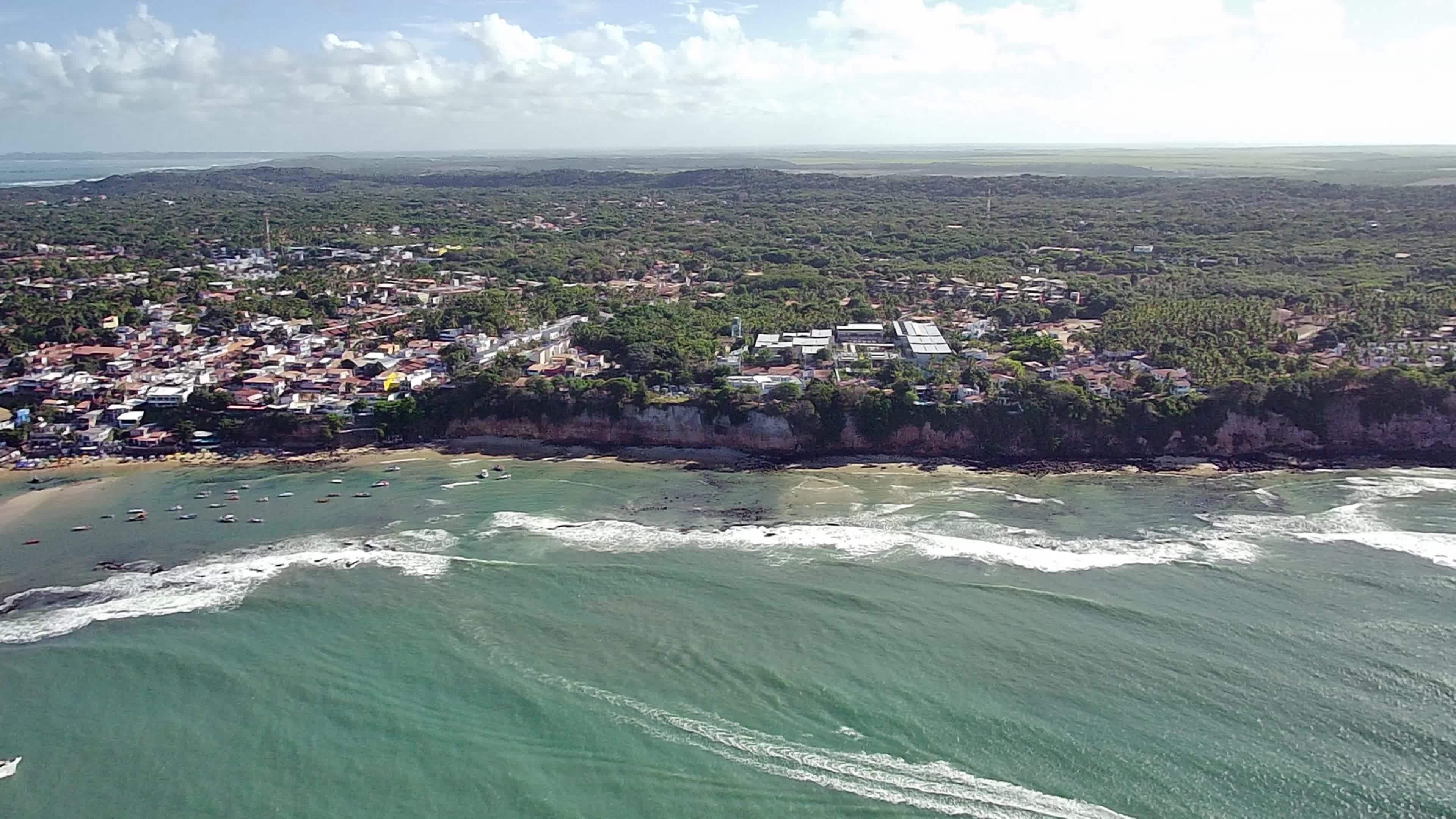 An aerial view of a coastal town with a beach, ocean, and surrounding hills.