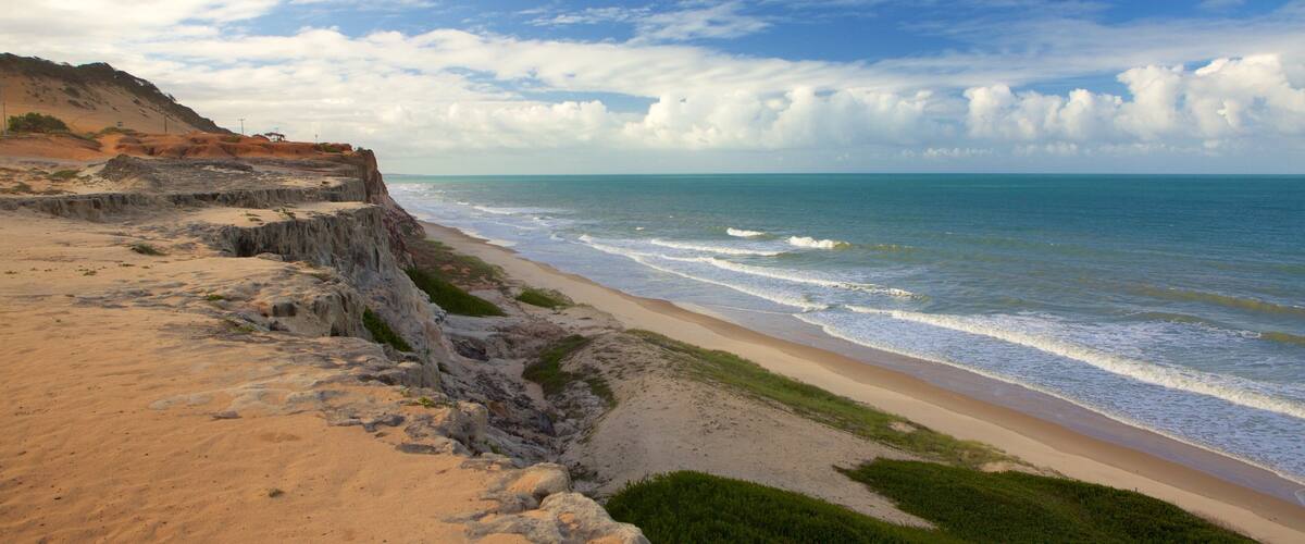 A coastal landscape with a sandy beach, rocky cliffs, and the ocean.