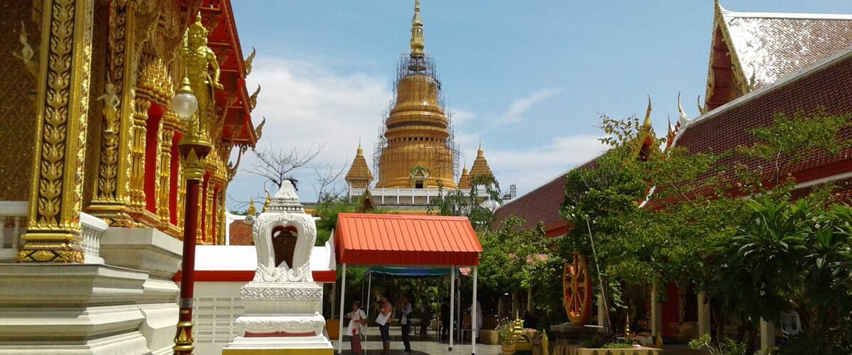 A temple with golden spires and a large central stupa, surrounded by ornate buildings and a paved walkway.
