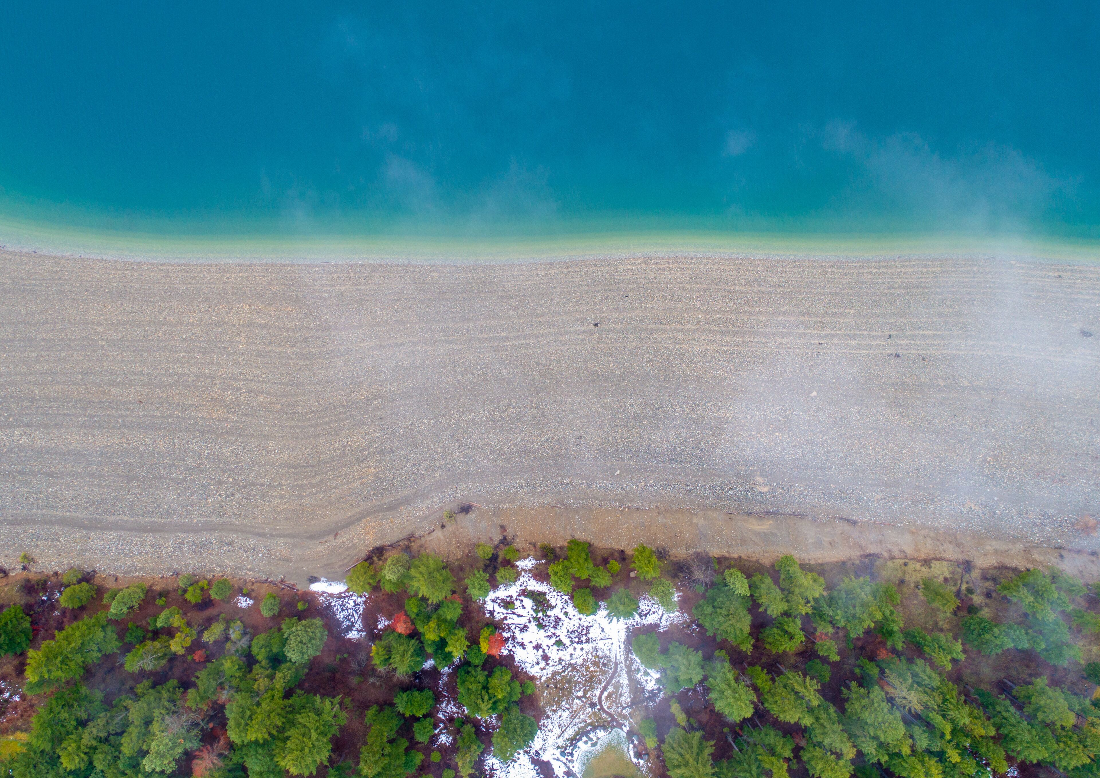 An aerial view of a beach with clear turquoise water, a sandy shore, and a forested area at the water's edge.