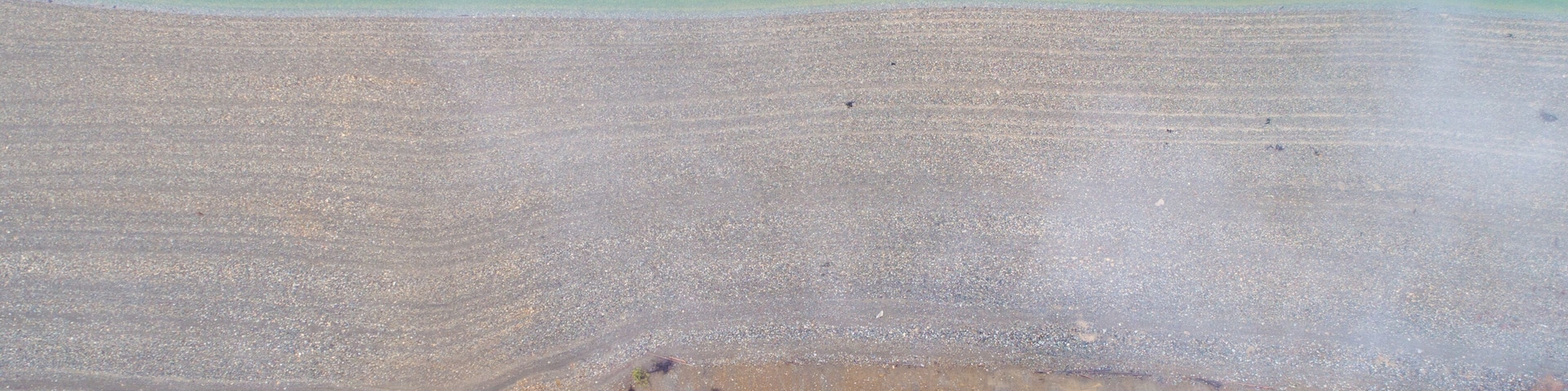 An aerial view of a beach with clear turquoise water, a sandy shore, and a forested area at the water's edge.