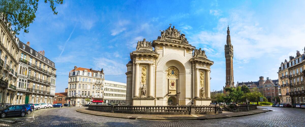 A historic monument with intricate sculptures, a tall clock tower, and surrounding classic European architecture.