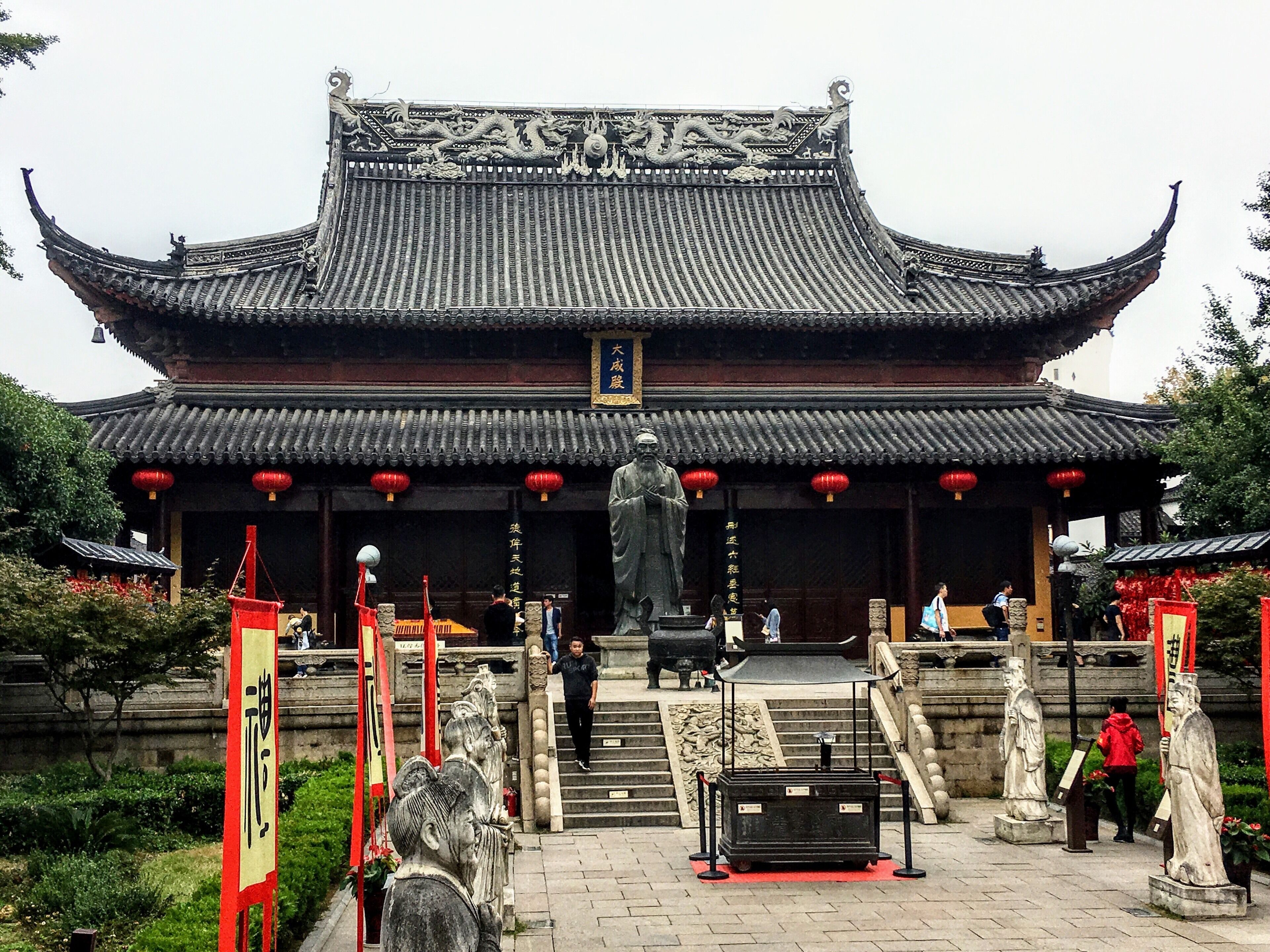 A traditional Chinese building with ornate roof tiles and a large statue in front.