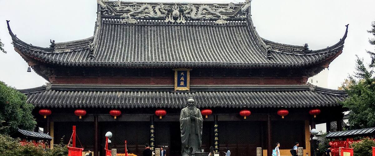 A traditional Chinese building with ornate roof tiles and a large statue in front.