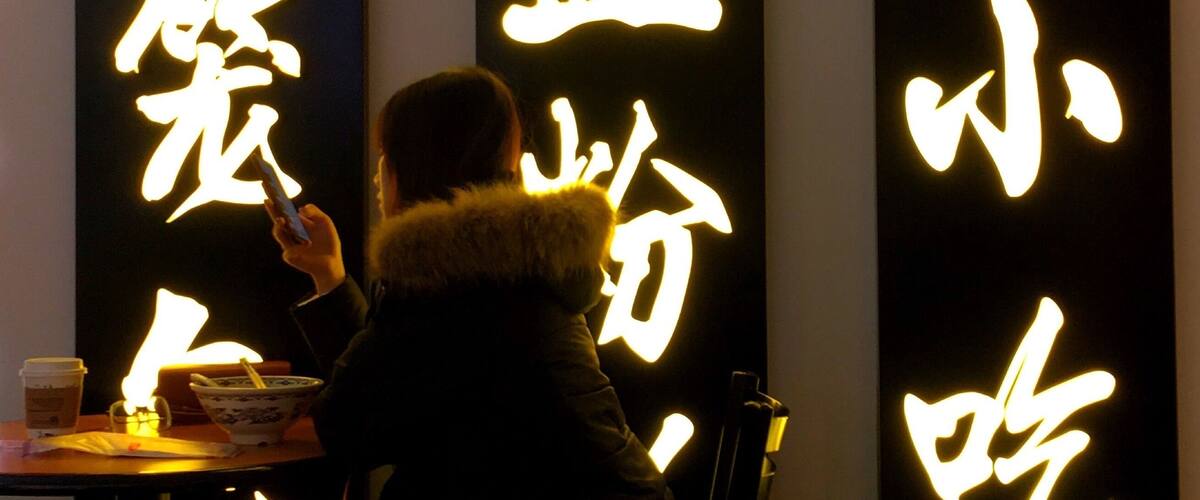 A person sitting at a table with illuminated Chinese characters on the wall behind them.