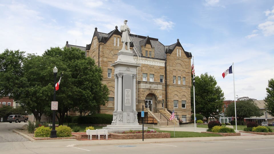 A historic building with a statue in front, surrounded by trees and a flag.