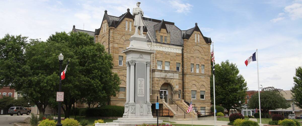 A historic building with a statue in front, surrounded by trees and a flag.
