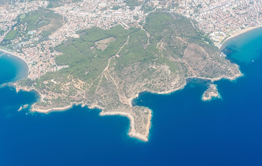 Une vue aérienne d’une ville côtière, avec des zones urbaines densément peuplées, des parcs verdoyants et une vaste étendue d’eau.