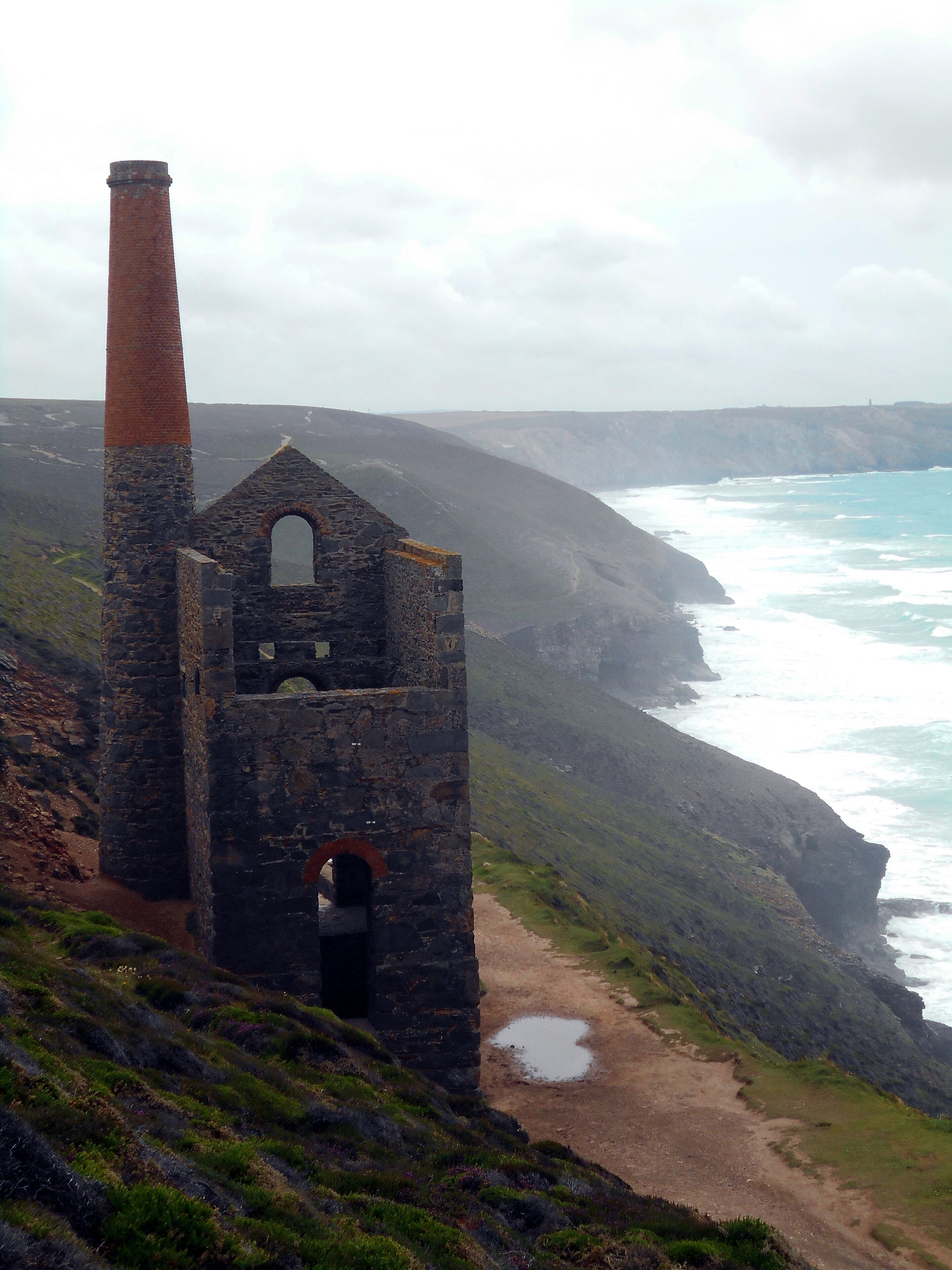 A coastal cliff with a stone structure featuring a chimney and an arched entrance.