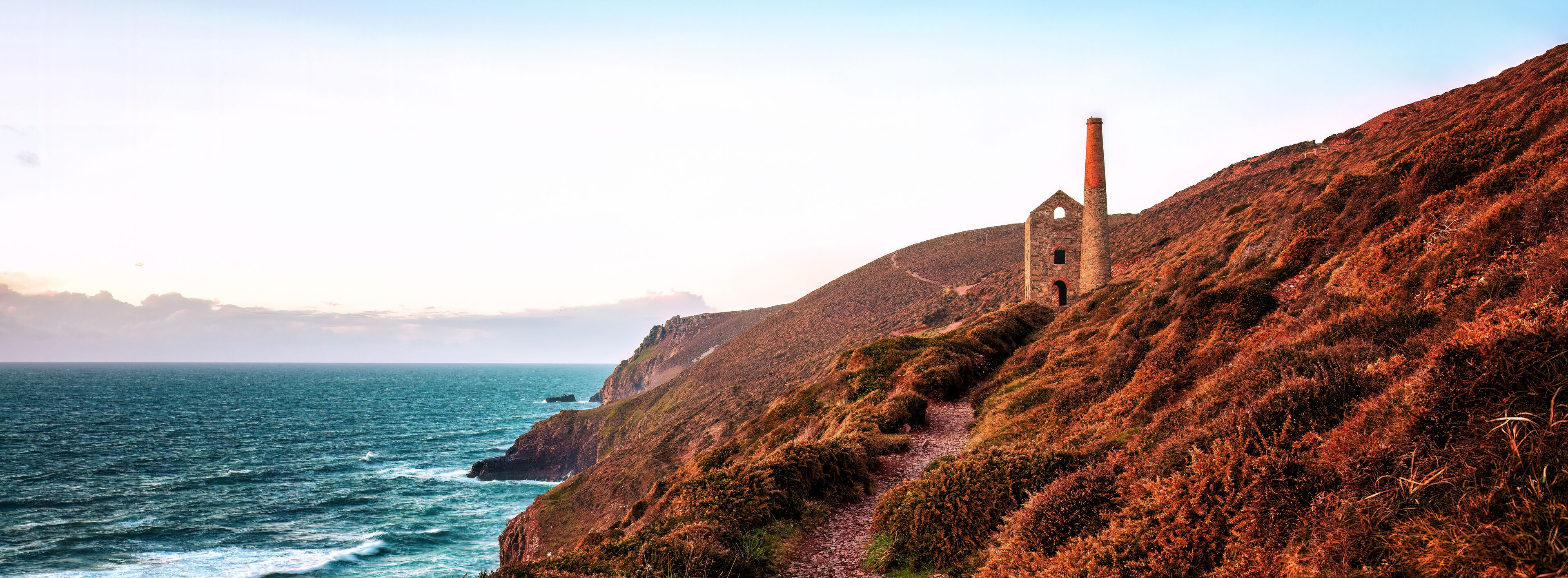 A coastal landscape with a red brick chimney, a dilapidated building, and a rugged coastline.