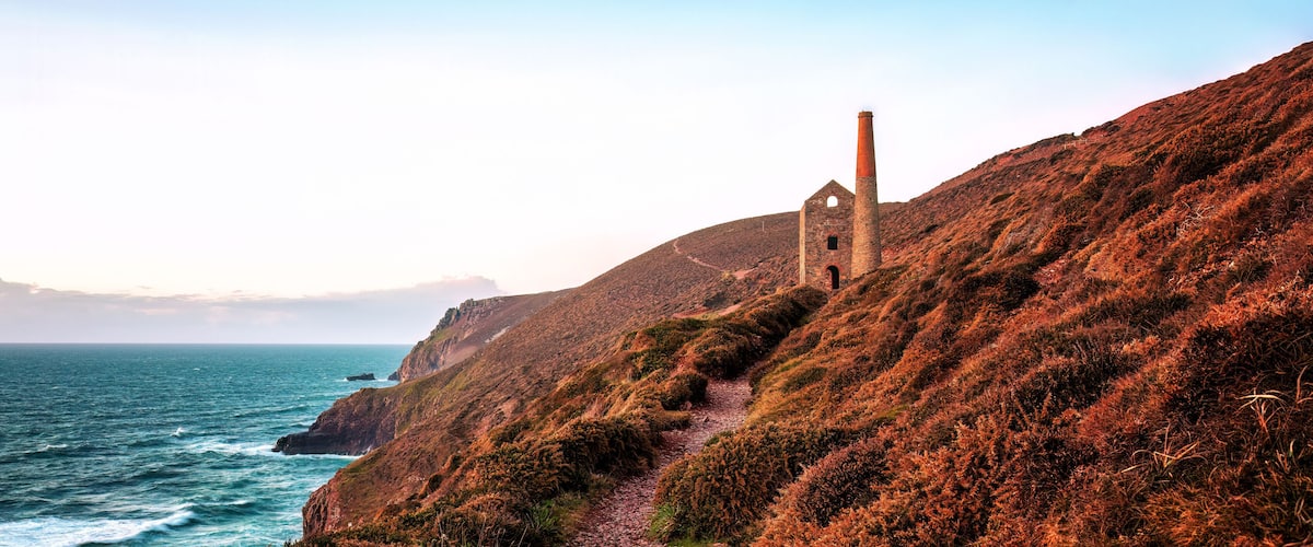 A coastal landscape with a red brick chimney, a dilapidated building, and a rugged coastline.