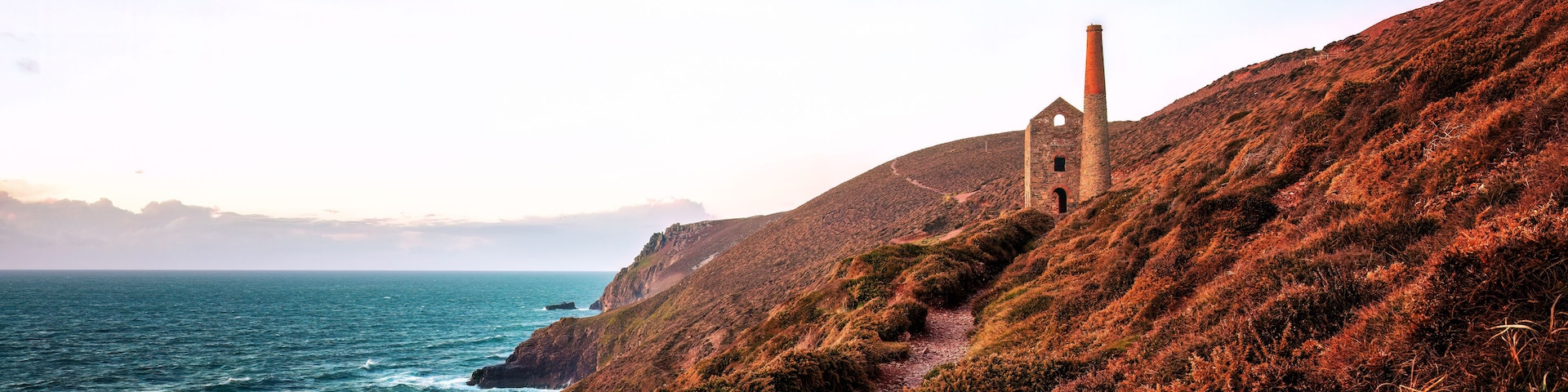 A coastal landscape with a red brick chimney, a dilapidated building, and a rugged coastline.