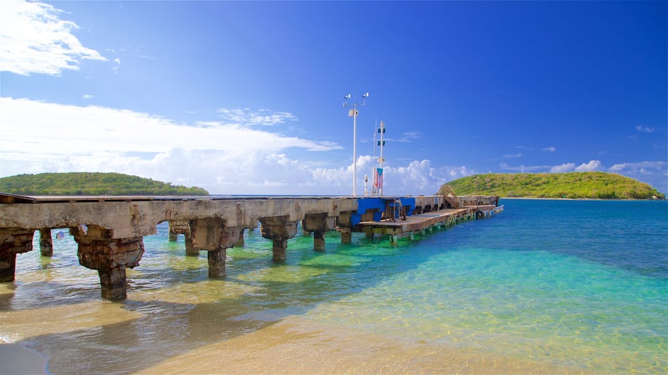 Une jetée s’avançant dans des eaux turquoise, sous un ciel dégagé, avec une île verdoyante en arrière-plan.