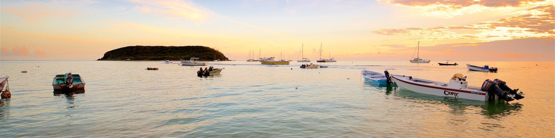 A calm sea with several boats anchored near a sandy beach.