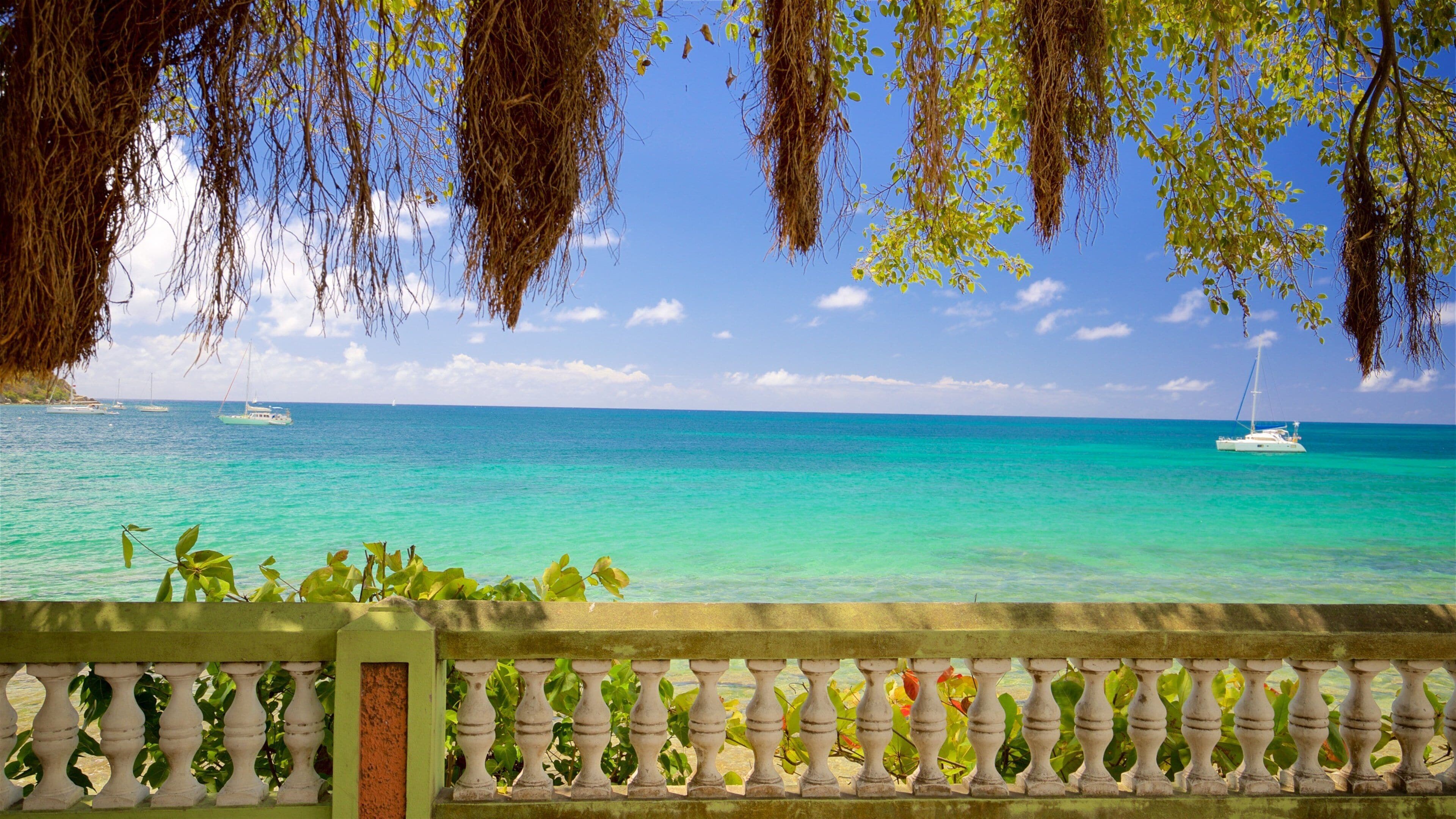 A turquoise sea with boats, a clear sky, and a balcony with plants.