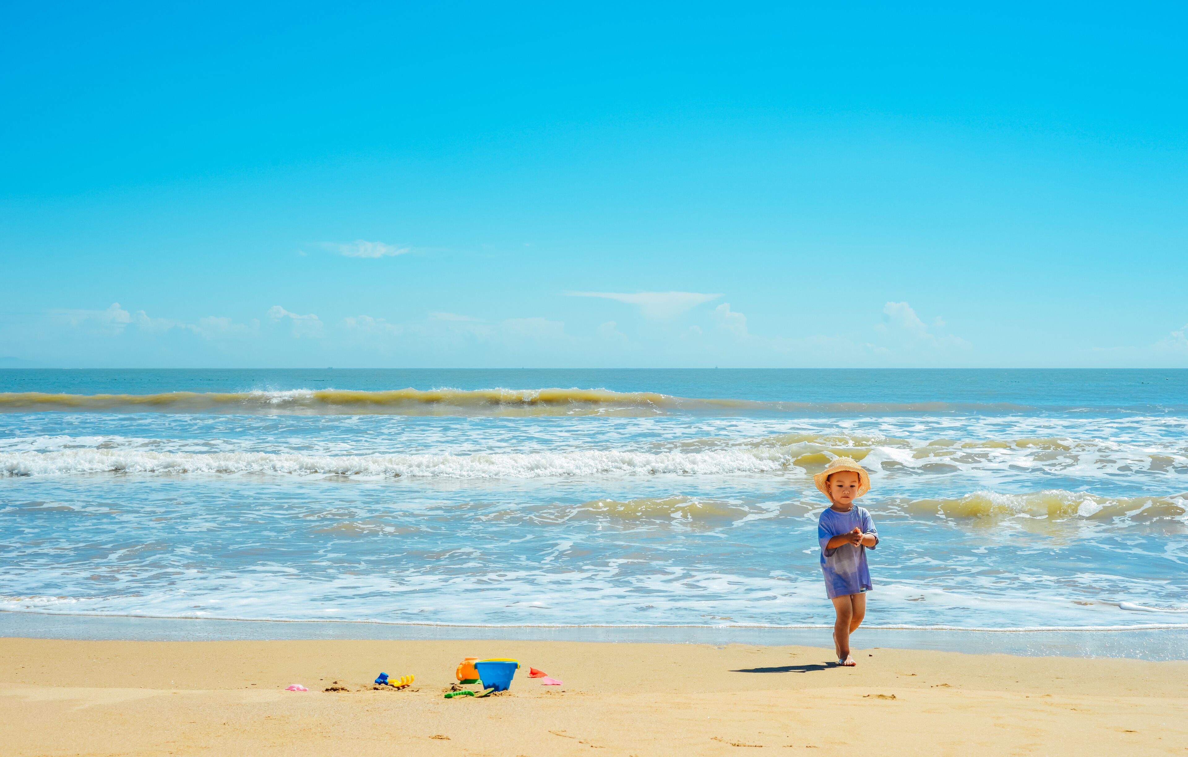 A child on a sandy beach with the ocean in the background.