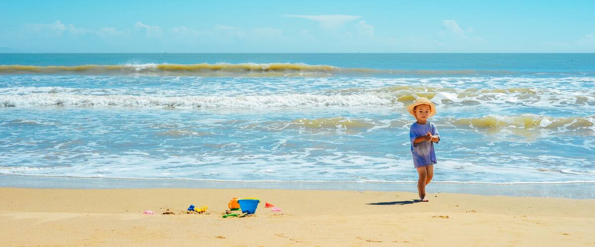A child on a sandy beach with the ocean in the background.