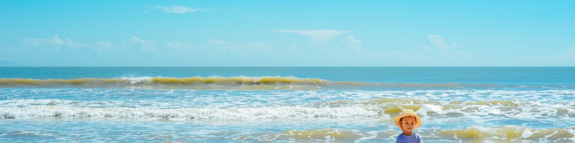 A child on a sandy beach with the ocean in the background.