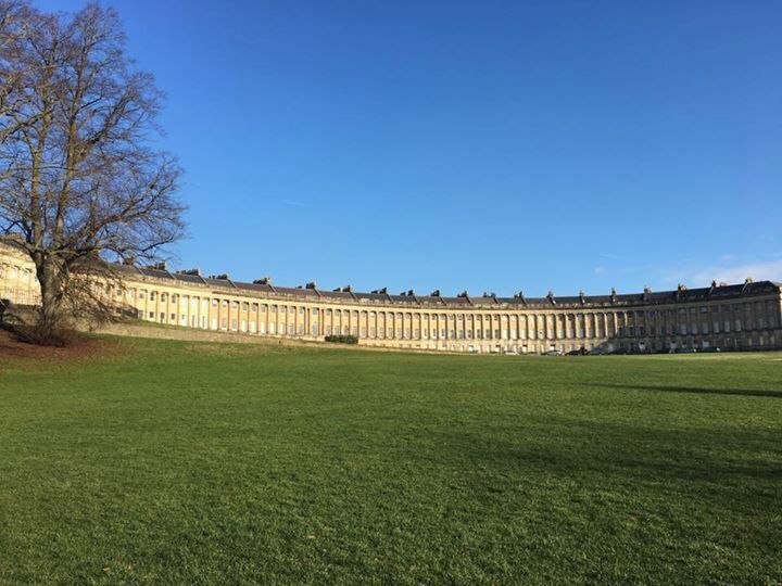 A large classical building with a symmetrical facade, a well-maintained lawn, and a leafless tree.