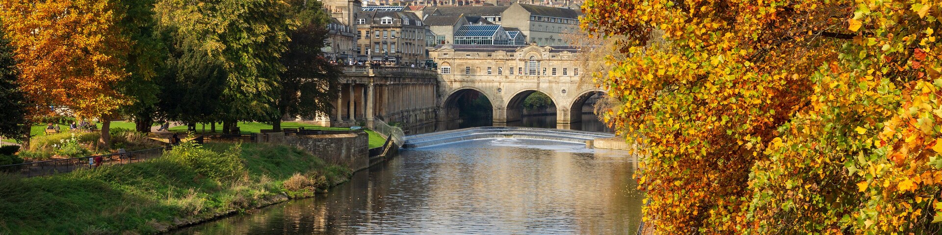 Un río con un puente, árboles otoñales y edificios históricos.