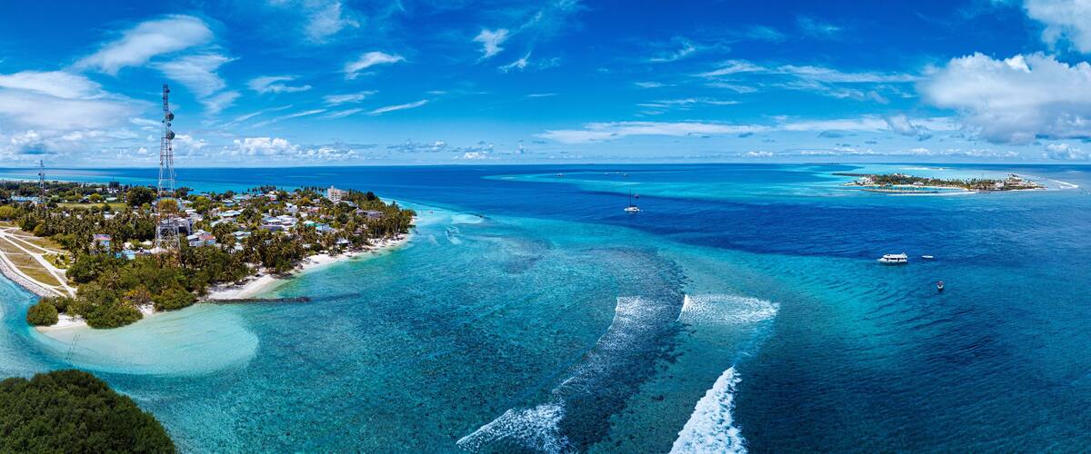 A tropical island with clear turquoise waters, a lighthouse, and a small boat in the distance.