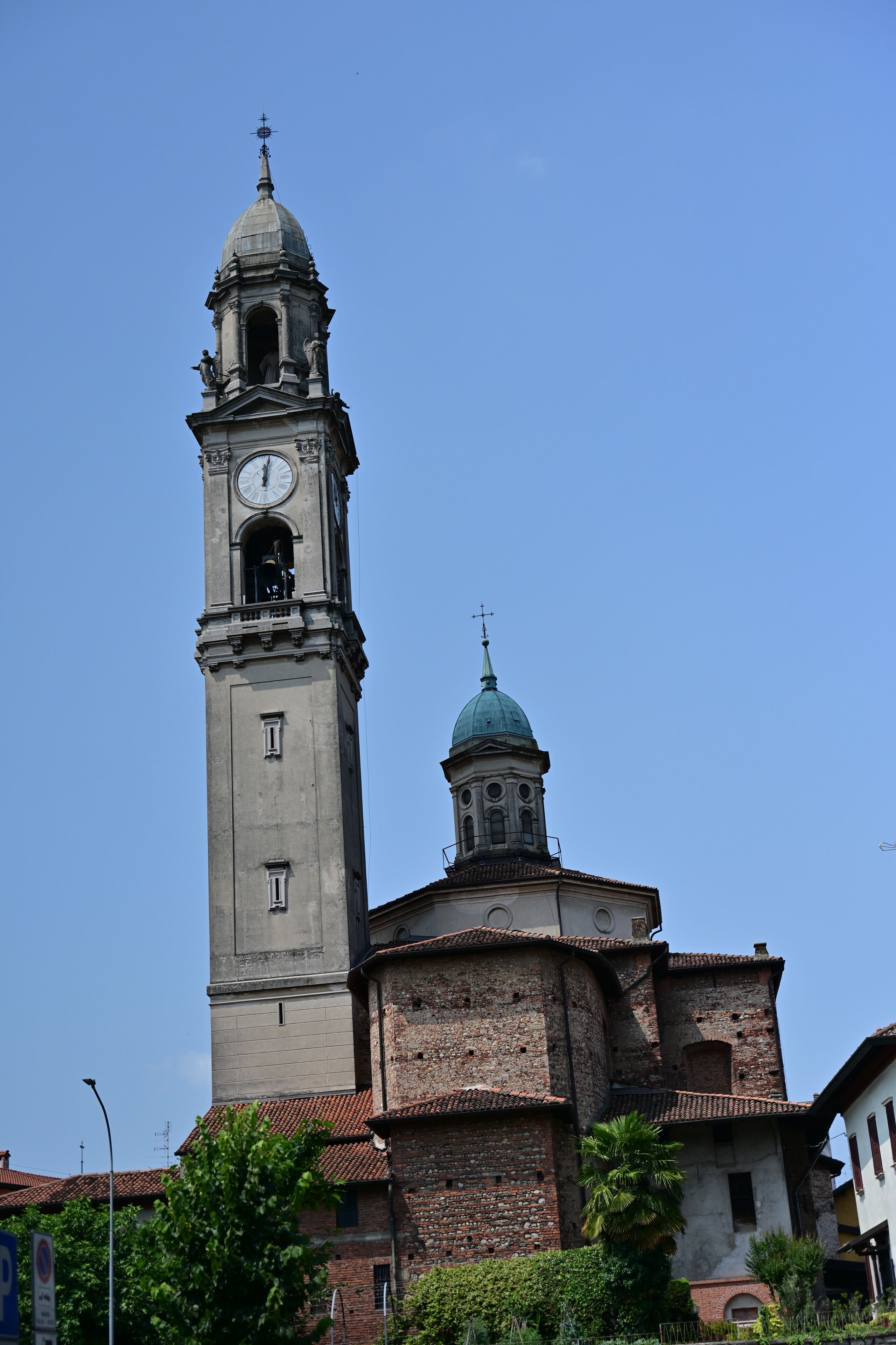 A tall clock tower with a dome and a smaller spire, surrounded by buildings and greenery.