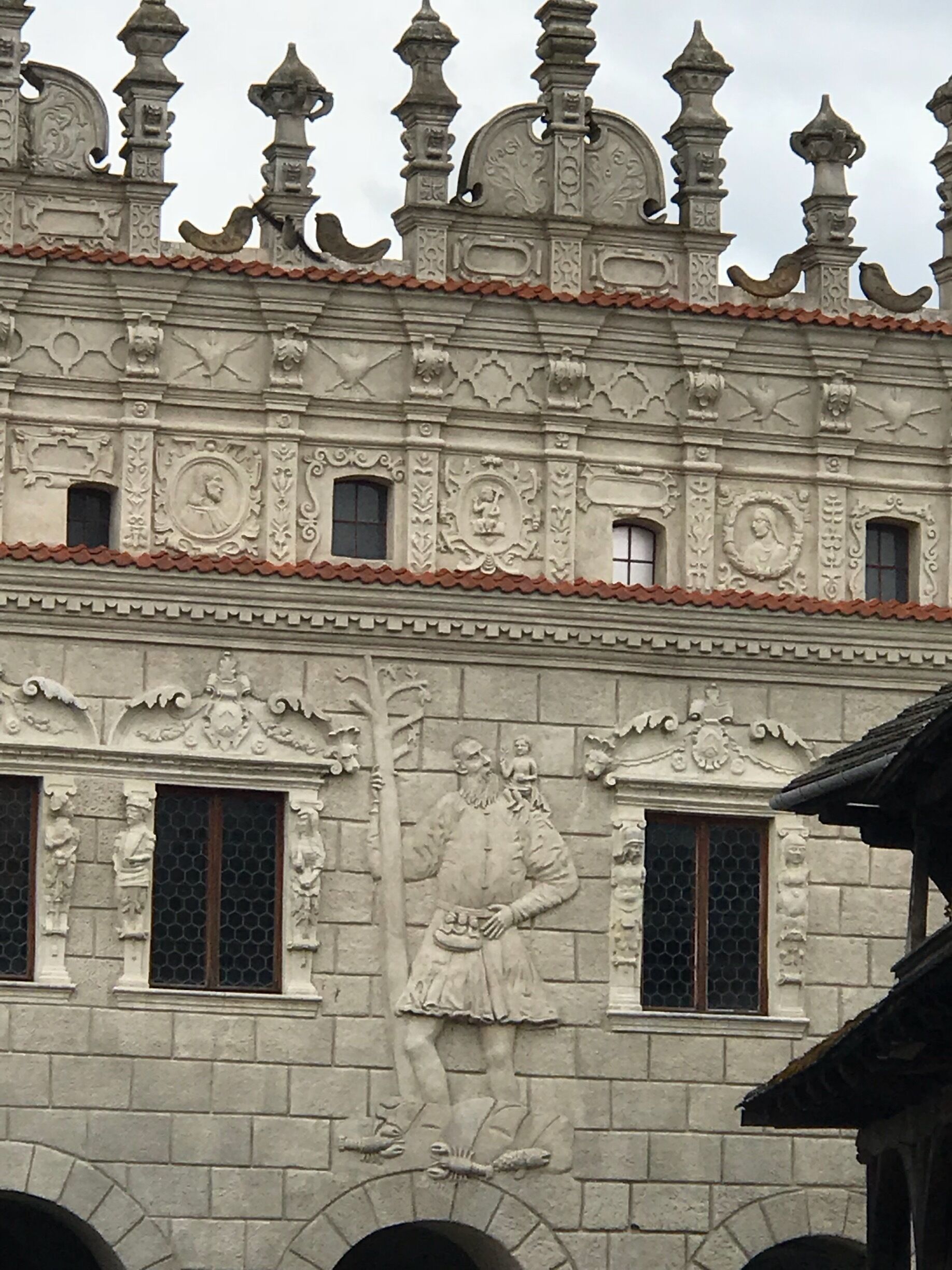 A building with ornate architectural details, including a large relief sculpture of a man and child, and decorative elements on the roof.