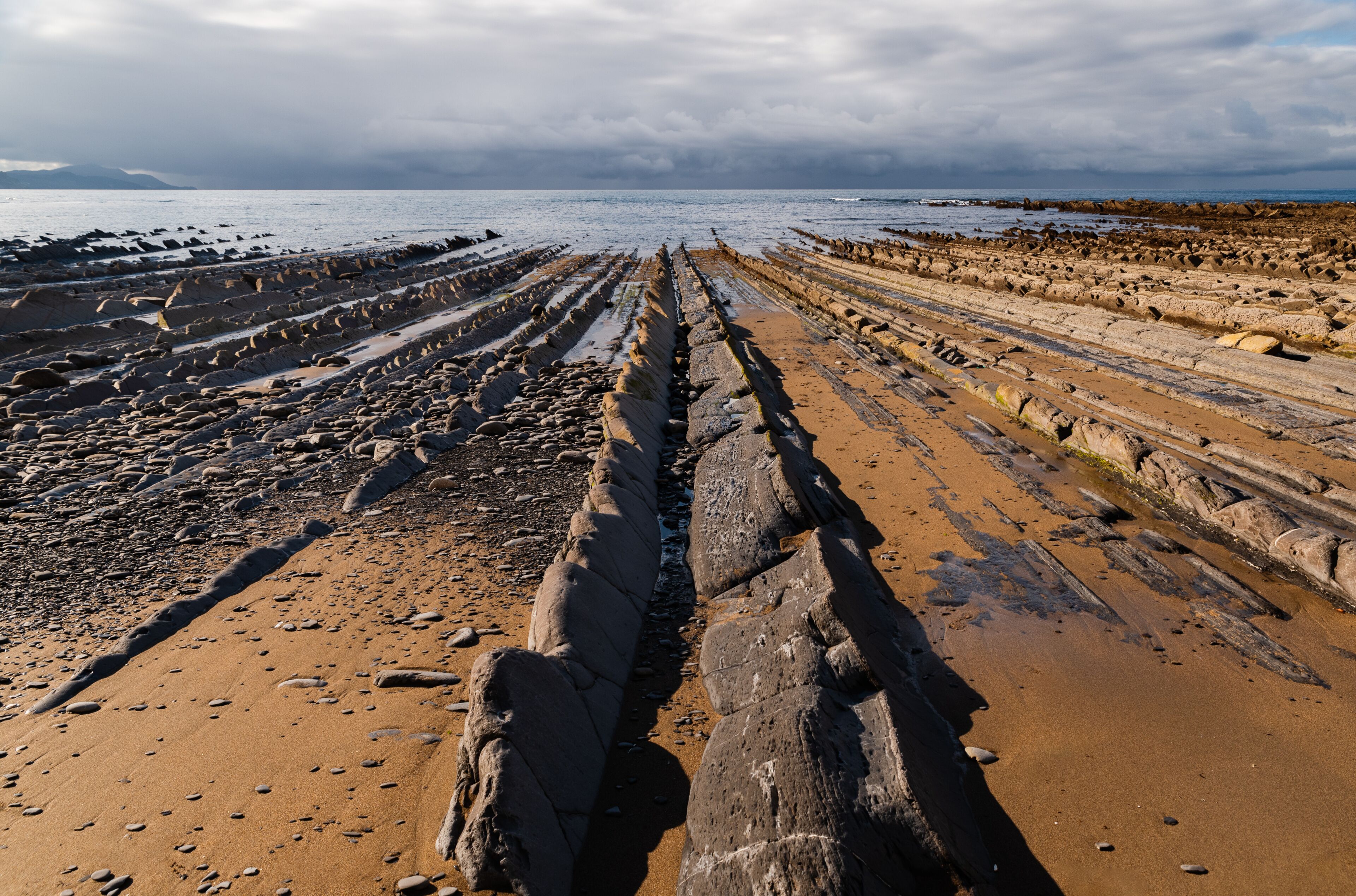 Une plage rocheuse où l’on trouve des formations rocheuses sédimentaires en couches qui s’étendent jusqu’à la mer.