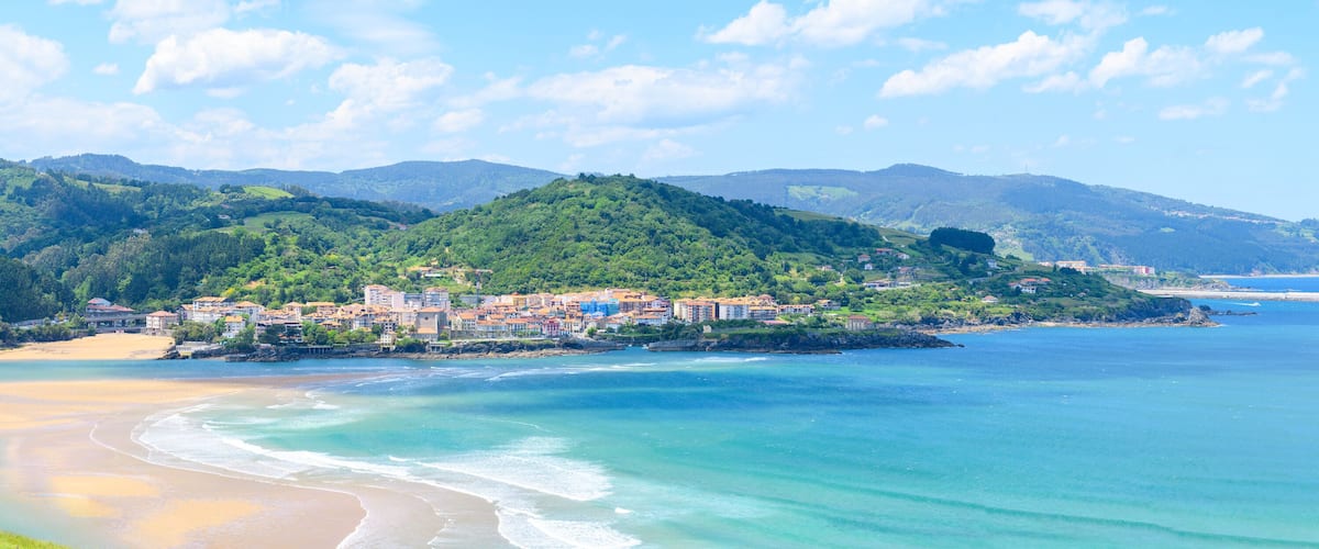 A coastal town with buildings on a hillside, a beach, and a clear blue sea.