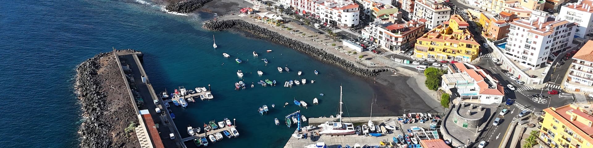 An aerial view of a coastal town with a marina, rocky breakwater, and colorful buildings.