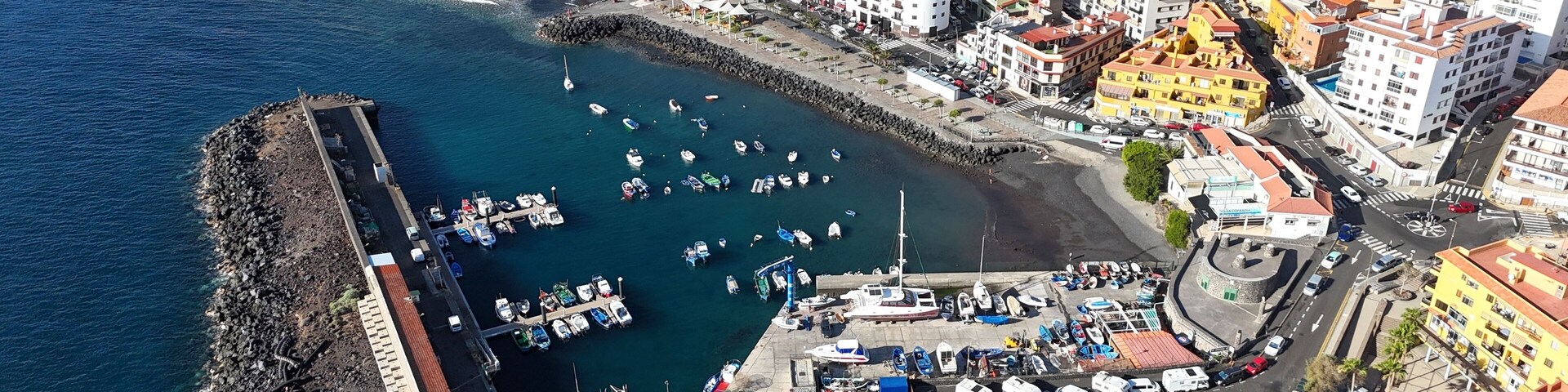 An aerial view of a coastal town with a marina, rocky breakwater, and colorful buildings.