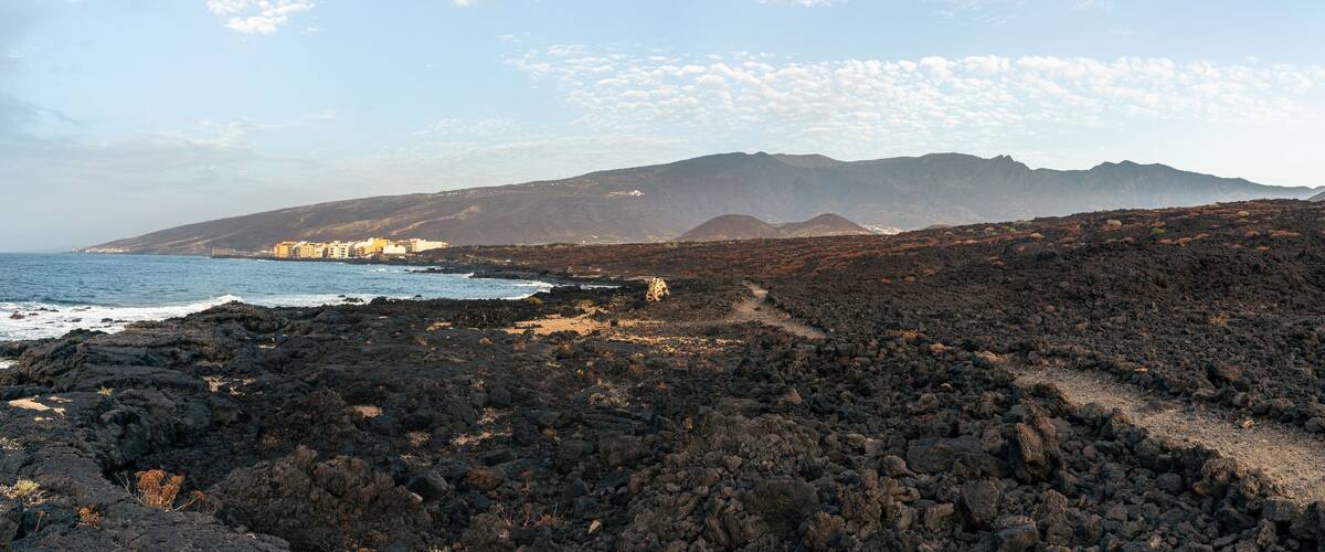 A coastal landscape with rocky terrain, a beach, and a mountain range in the background.
