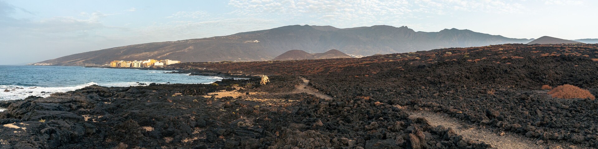 A coastal landscape with rocky terrain, a beach, and a mountain range in the background.
