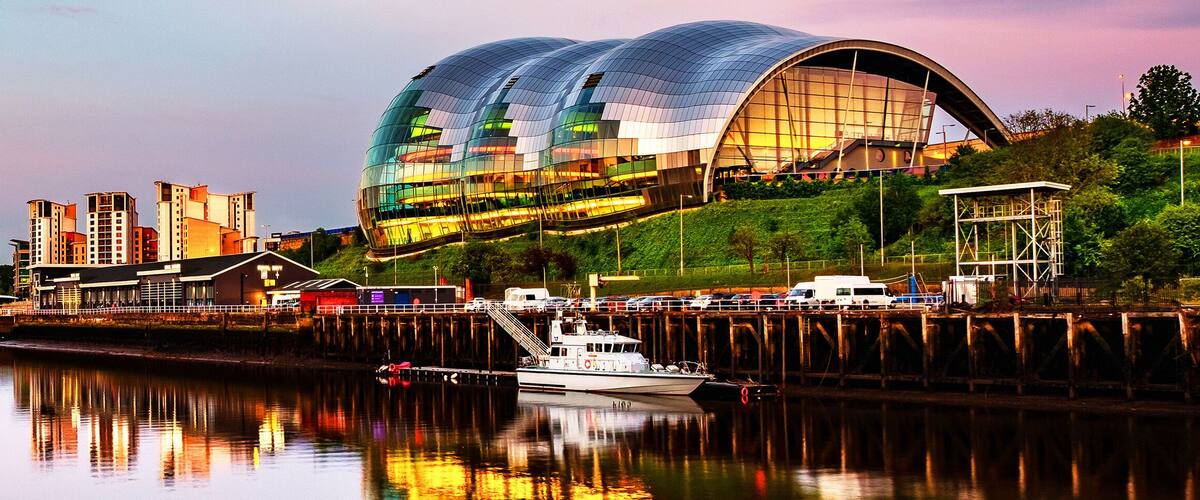 A waterfront cityscape with a modern bridge, a large stadium, and a boat docked near the river.