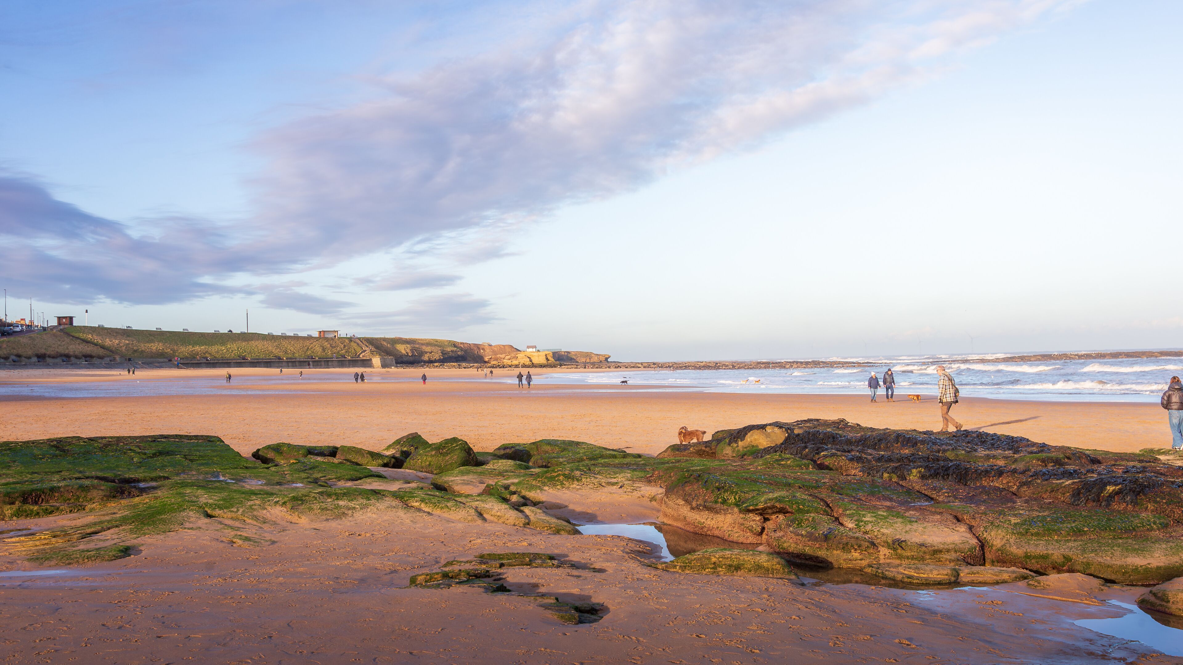 A beach with rocky outcrops, waves, and a distant cliff.