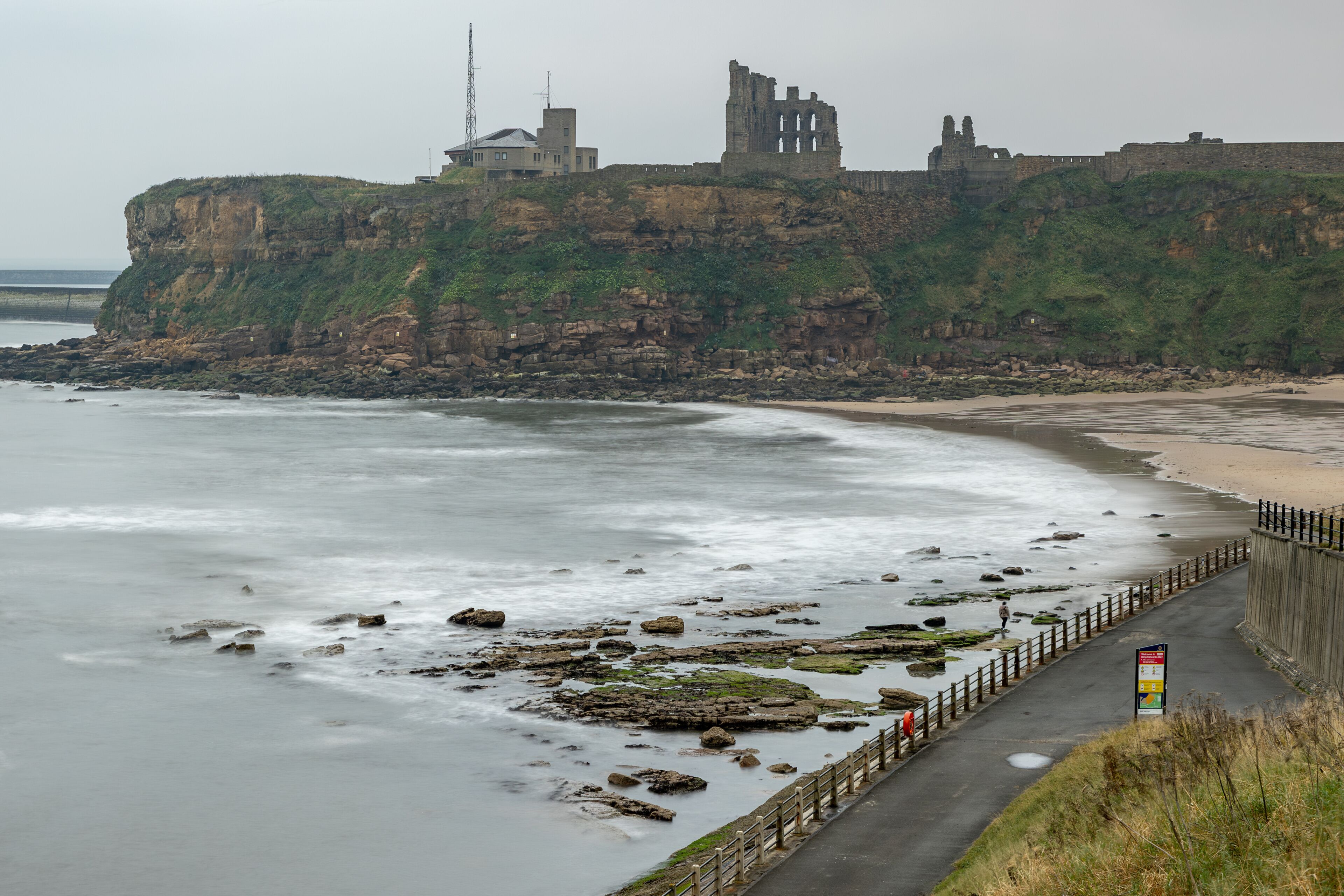 A coastal landscape with a cliff, a ruined castle, and a beach.