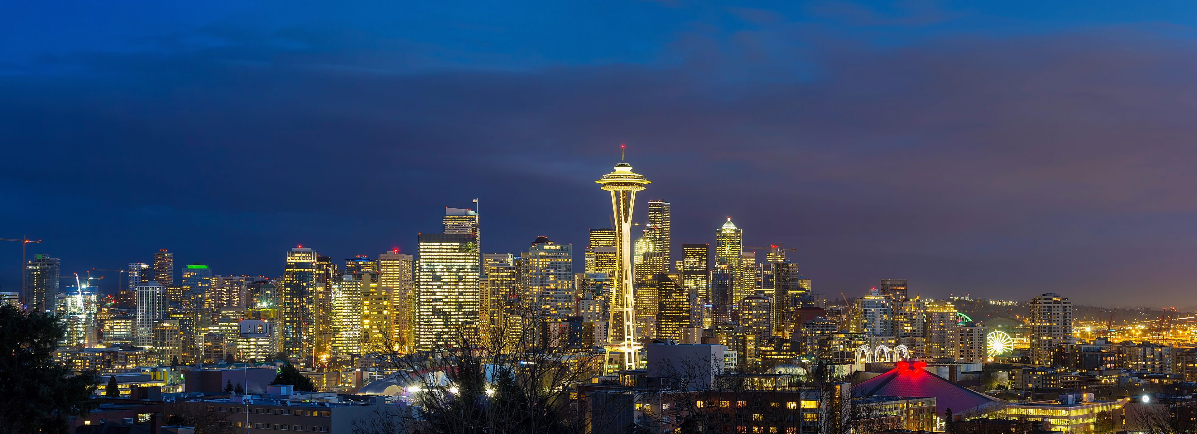 A city skyline at night with illuminated buildings and the Space Needle as a prominent landmark.