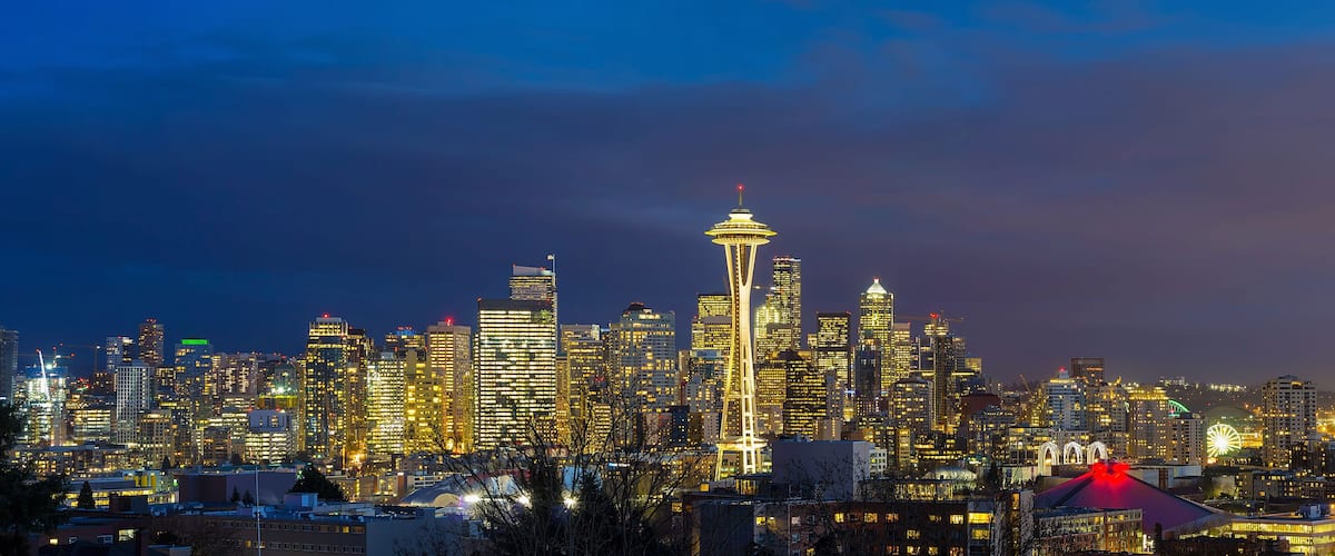 A city skyline at night with illuminated buildings and the Space Needle as a prominent landmark.