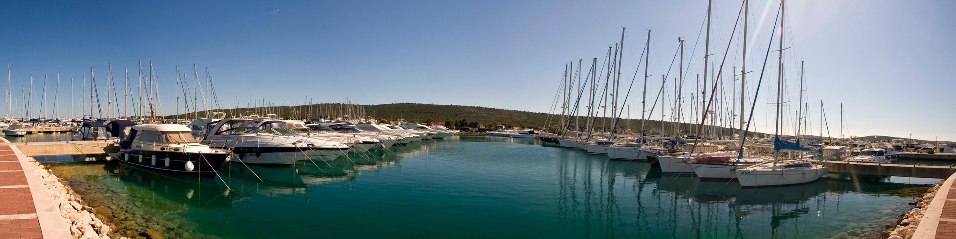 A marina with numerous sailboats docked along a calm waterfront.