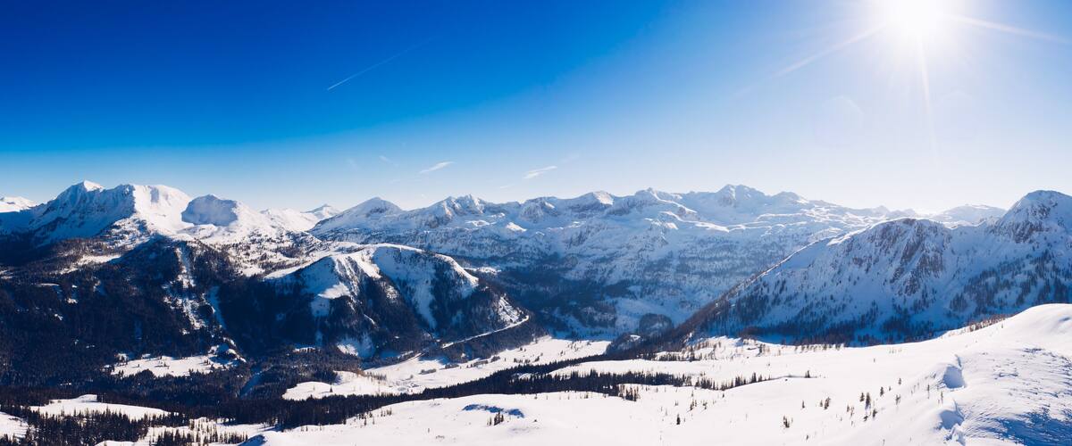 A snow-covered mountain range with a clear sky and a bright sun.