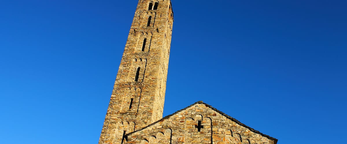 A tall stone tower with a steep roof and a shorter building with arched windows.