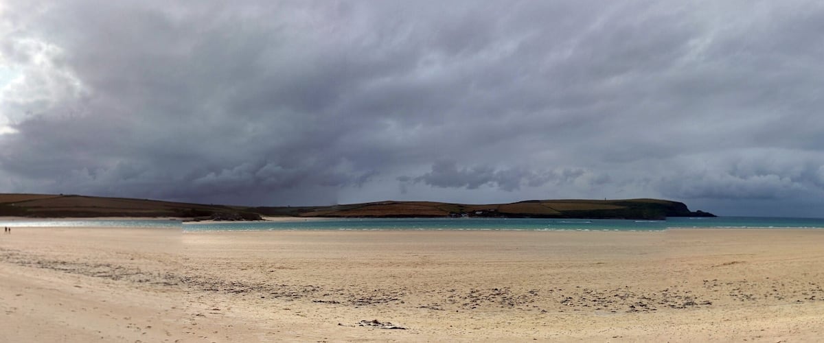 A beach with a stormy sky, distant hills, and a calm sea.