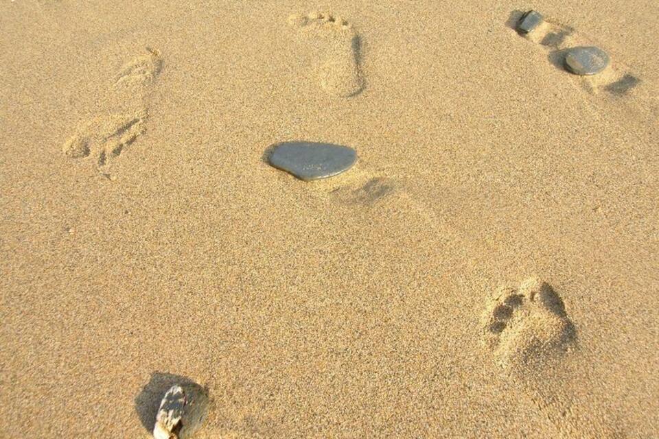 Petjades i una pedra a la sorra de la platja.
