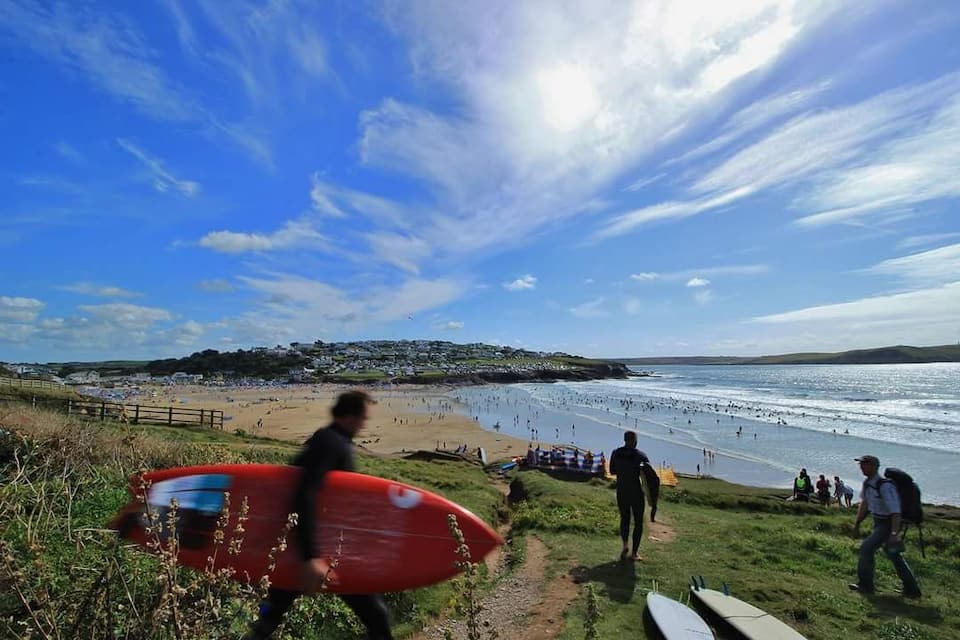 A beach with people walking and carrying surfboards, a sandy shore, and a distant town.