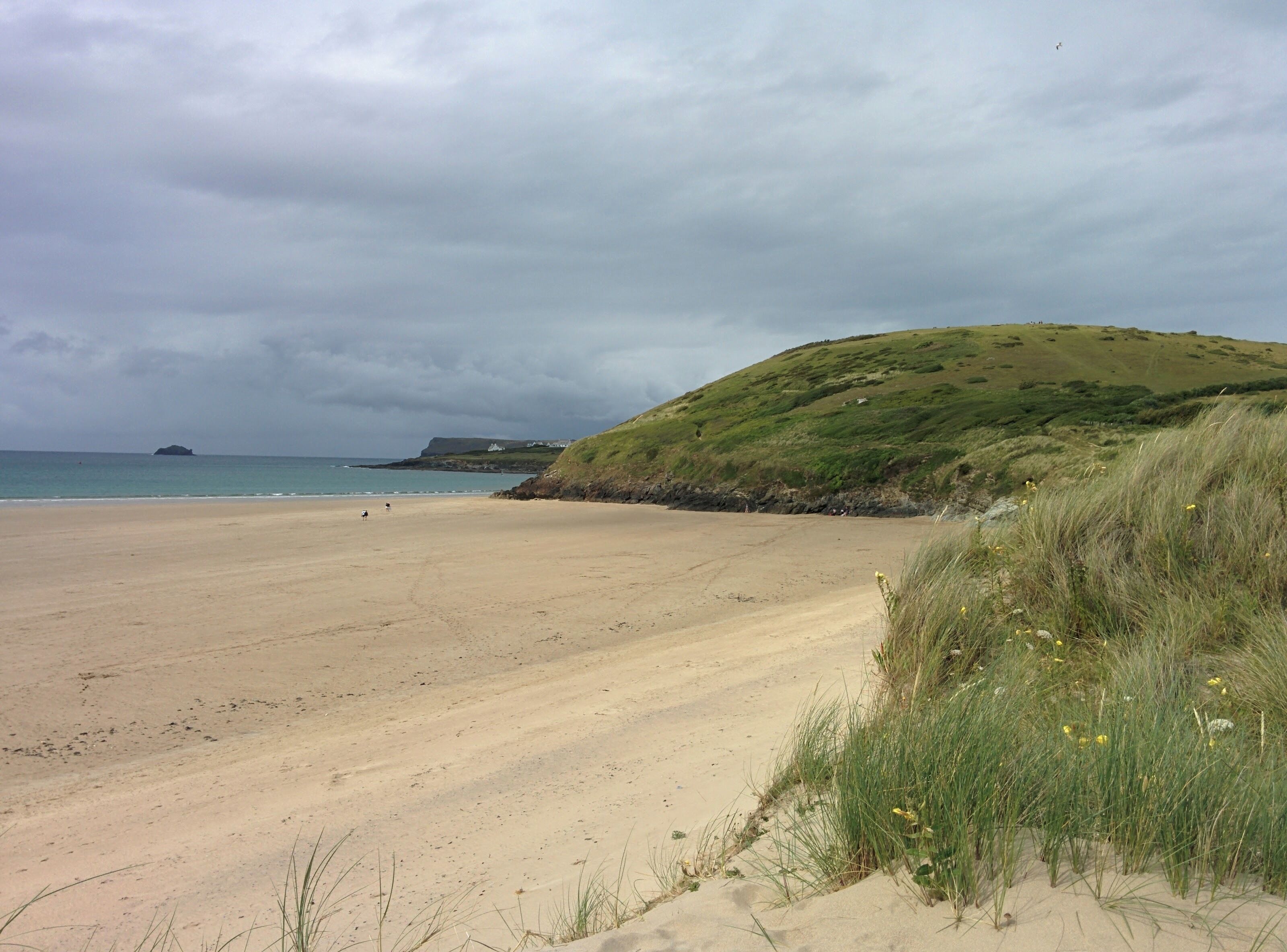 A sandy beach with a grassy hill and a body of water in the background.