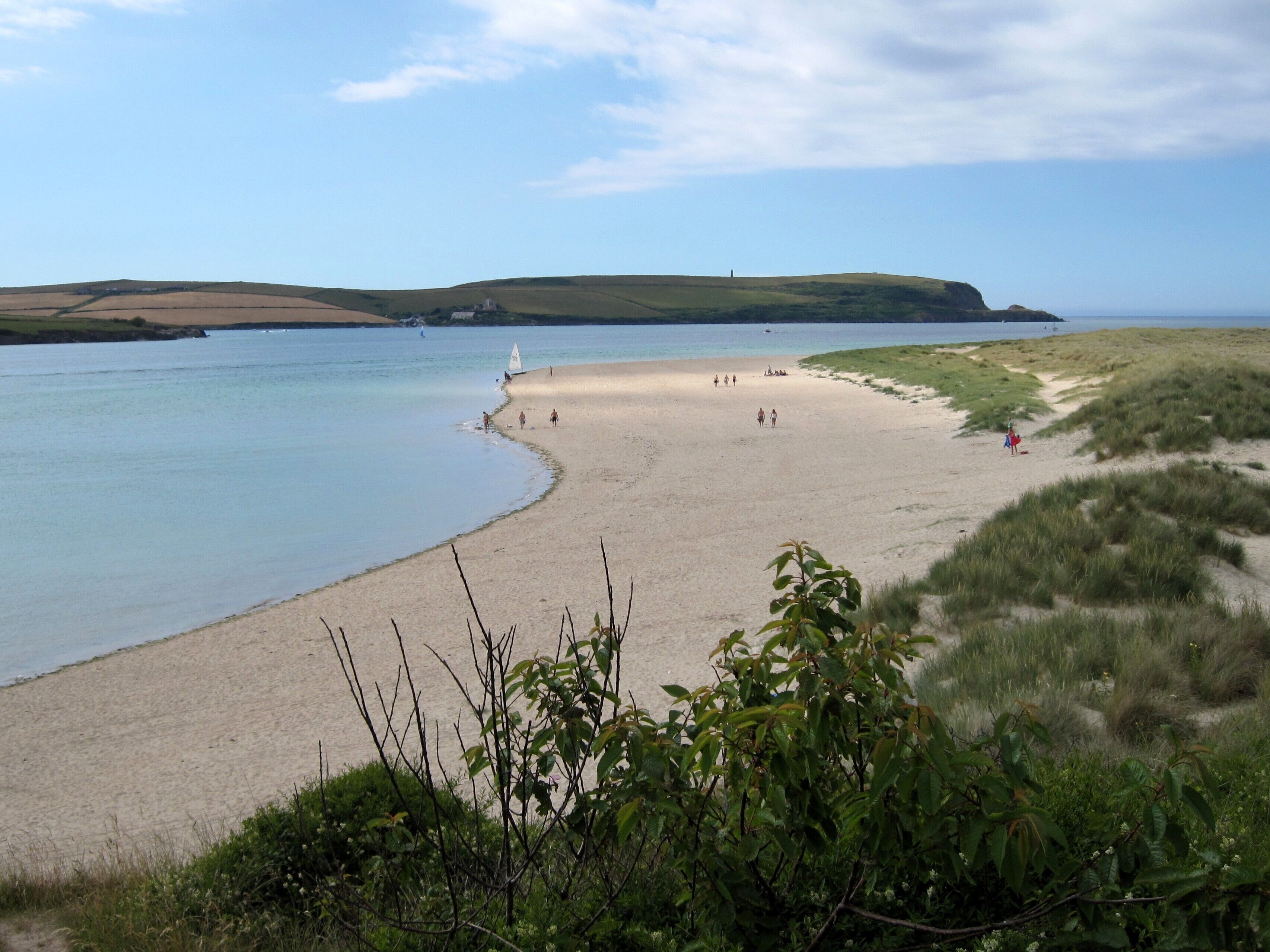 A beach with gentle waves, grassy dunes, and a distant hill.